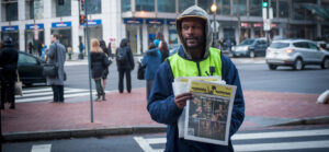 man in neon vest handing out newspapers on the street